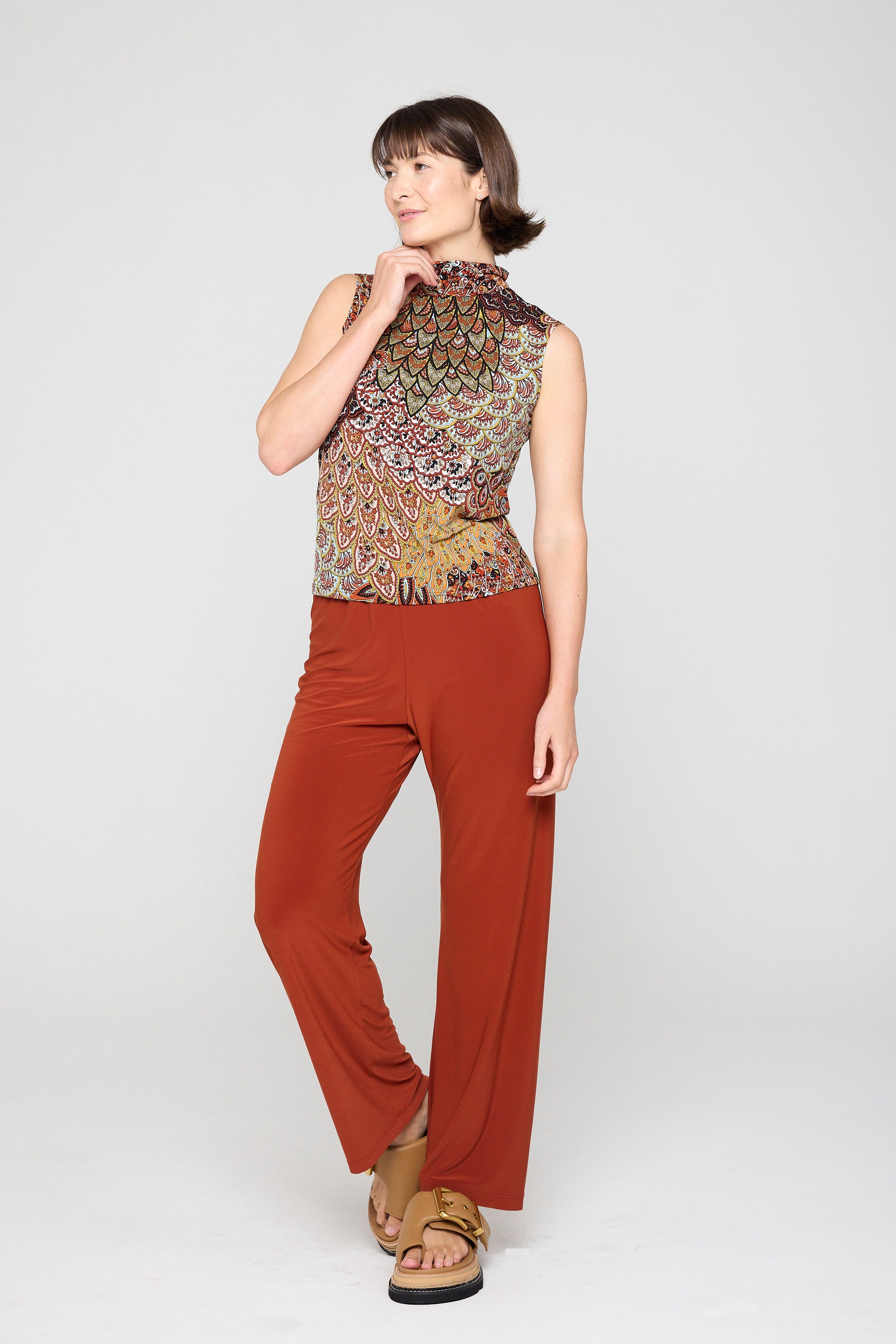 Woman wearing a patterned sleeveless top and red pants on a white background